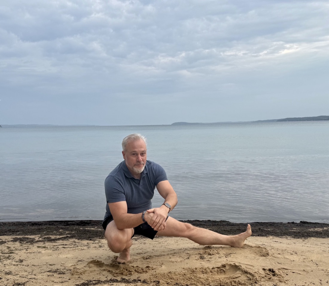 Philip Rosi in a side lunge on the beach at Grand Traverse Bay