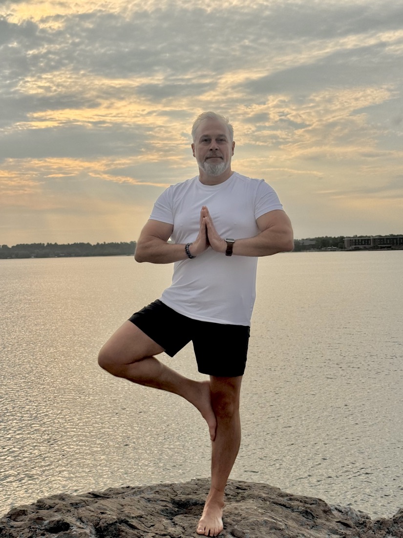 Philip Rosi in tree pose on a rock at the water's edge at sunset